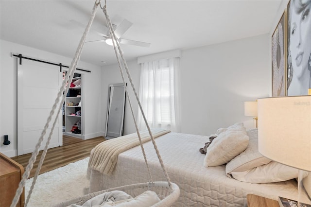 bedroom featuring a ceiling fan, a barn door, and wood finished floors