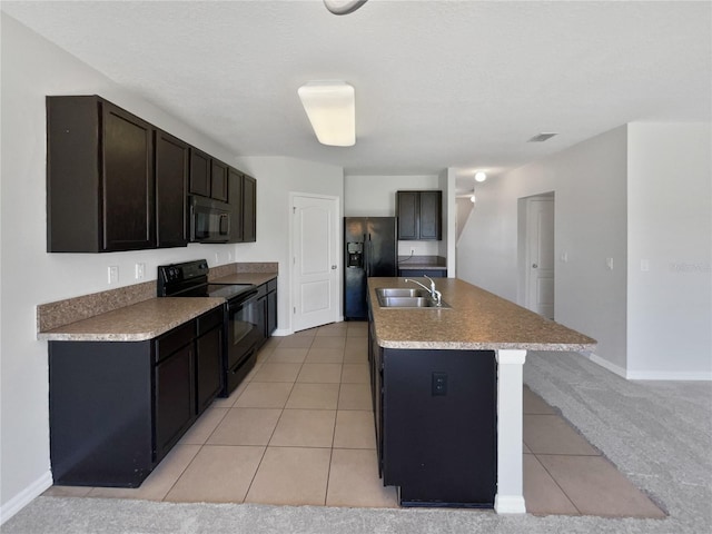 kitchen featuring black appliances, a kitchen island with sink, a sink, light tile patterned floors, and baseboards