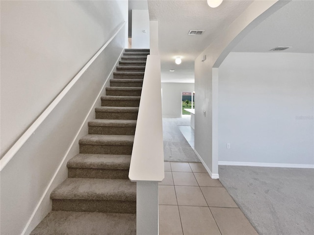 staircase with tile patterned floors, visible vents, arched walkways, carpet flooring, and baseboards