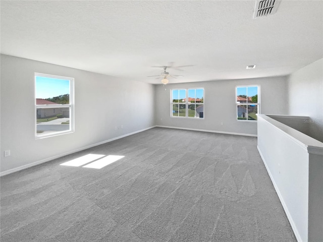 carpeted empty room featuring plenty of natural light, baseboards, visible vents, and ceiling fan