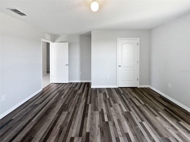 empty room featuring visible vents, baseboards, and dark wood finished floors