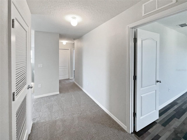 corridor with baseboards, visible vents, carpet floors, and a textured ceiling