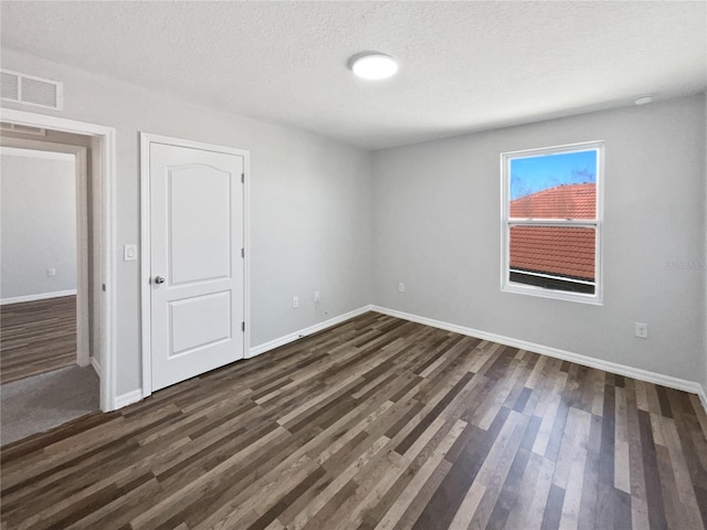 unfurnished room featuring dark wood finished floors, baseboards, visible vents, and a textured ceiling