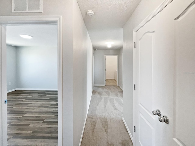 hallway featuring carpet flooring, baseboards, visible vents, and a textured ceiling