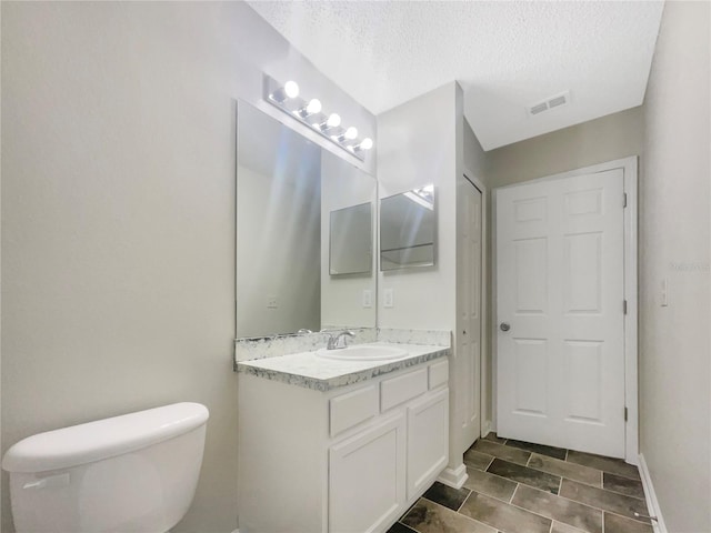 bathroom with vanity, baseboards, visible vents, a textured ceiling, and toilet