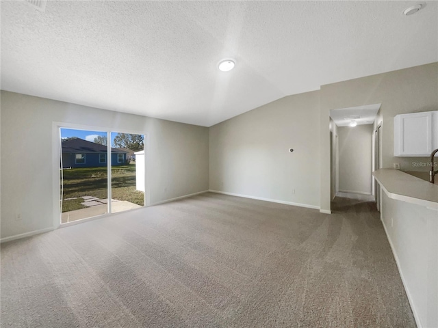 unfurnished living room with baseboards, lofted ceiling, light colored carpet, and a textured ceiling