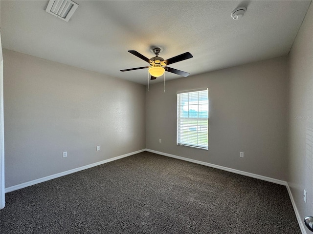 spare room featuring visible vents, baseboards, ceiling fan, a textured ceiling, and dark colored carpet