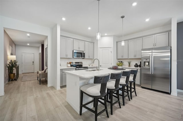 kitchen featuring light countertops, an island with sink, appliances with stainless steel finishes, light wood-style floors, and a sink