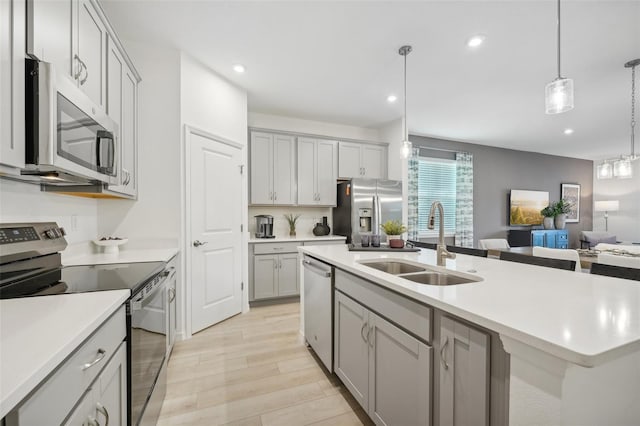 kitchen with gray cabinets, stainless steel appliances, light countertops, and a sink