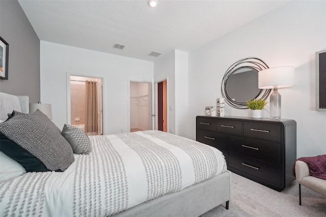 bedroom featuring a walk in closet, connected bathroom, visible vents, and light carpet