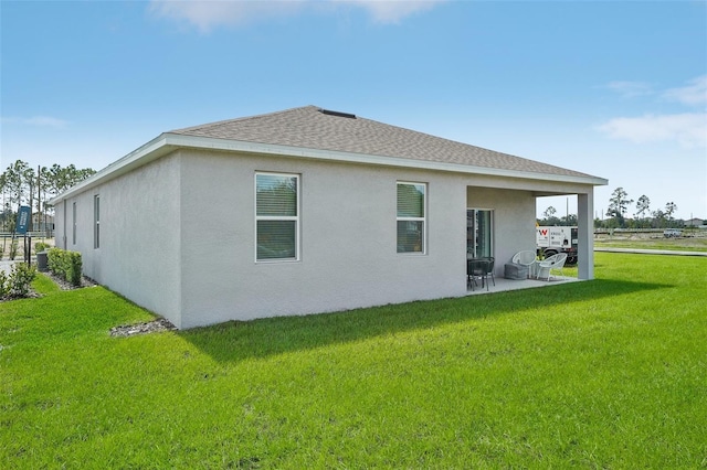 rear view of house with stucco siding, a patio, a yard, and roof with shingles