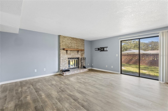 unfurnished living room featuring a brick fireplace, a textured ceiling, baseboards, and wood finished floors