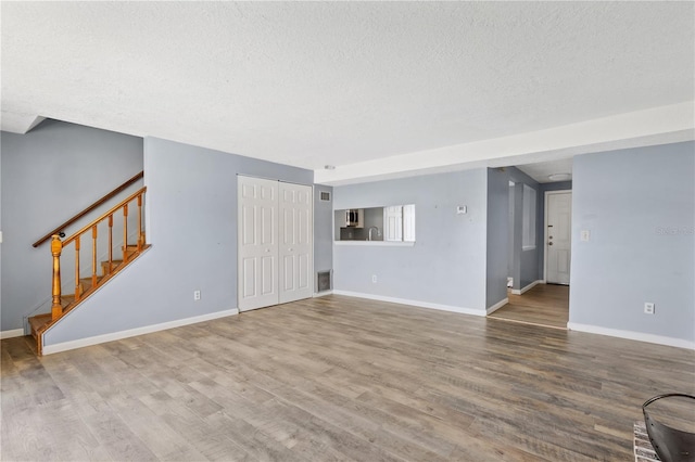 unfurnished living room with visible vents, baseboards, stairway, wood finished floors, and a textured ceiling