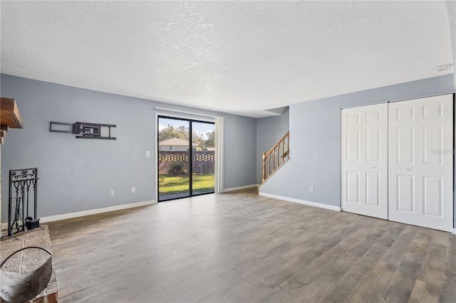 unfurnished living room featuring baseboards, a textured ceiling, wood finished floors, and stairs