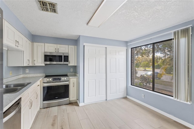 kitchen featuring visible vents, baseboards, light wood-type flooring, stainless steel appliances, and a sink