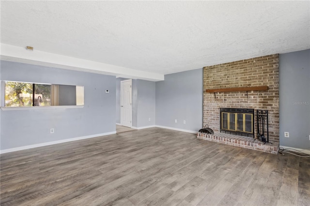 unfurnished living room with a fireplace, a textured ceiling, baseboards, and wood finished floors