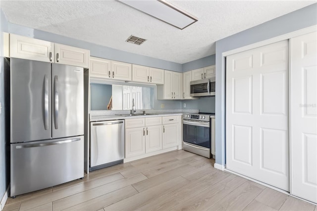 kitchen with visible vents, a sink, appliances with stainless steel finishes, light countertops, and wood tiled floor