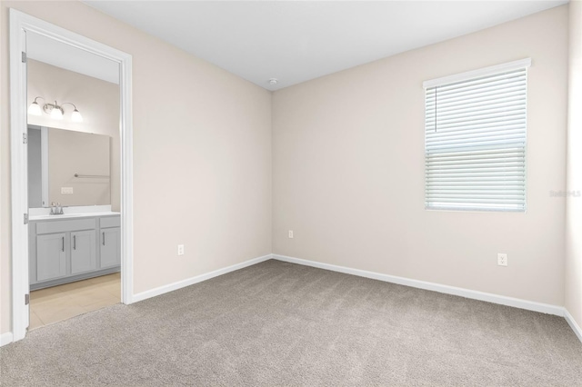 unfurnished bedroom with light carpet, ensuite bathroom, baseboards, and a sink