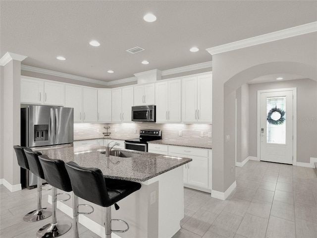 kitchen featuring light stone counters, arched walkways, stainless steel appliances, decorative backsplash, and a kitchen breakfast bar