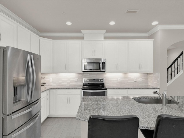 kitchen featuring a sink, arched walkways, appliances with stainless steel finishes, and white cabinets