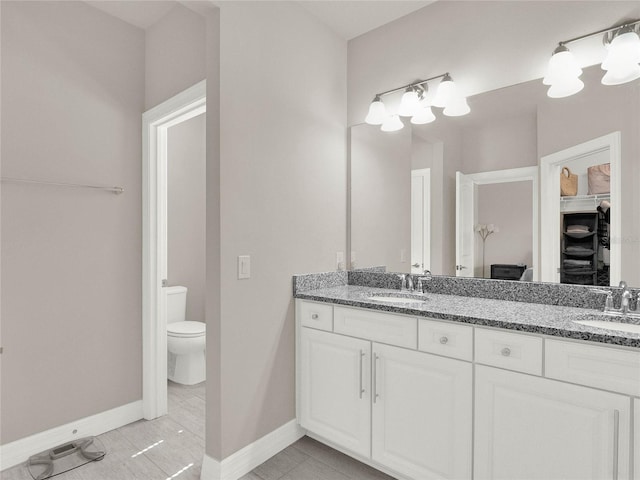 full bath featuring double vanity, toilet, baseboards, and a sink