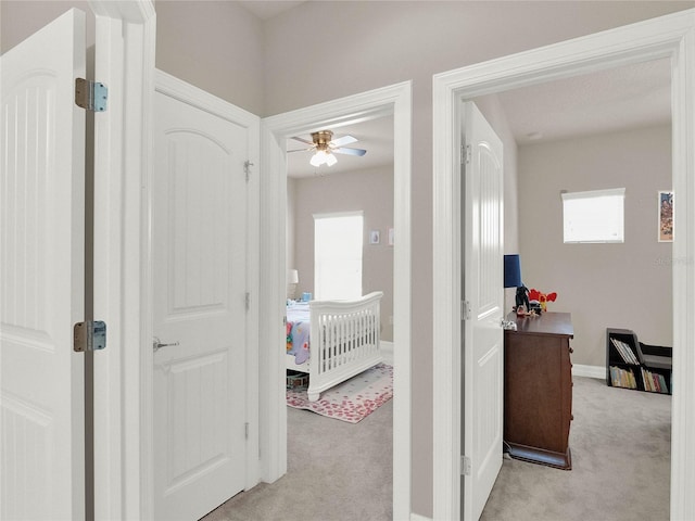 hallway featuring baseboards and light carpet