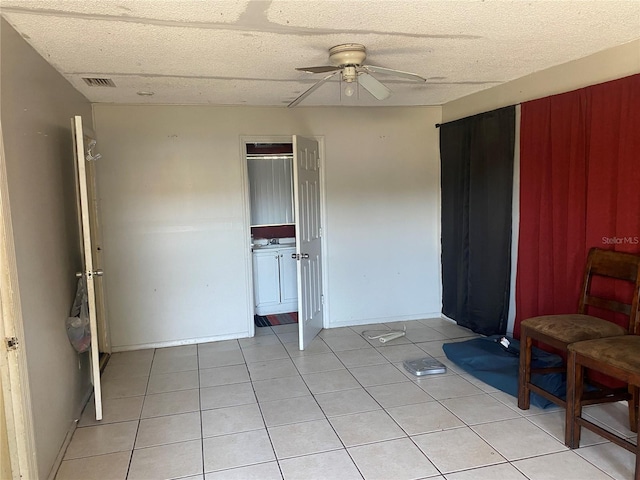 spare room featuring light tile patterned floors, visible vents, a textured ceiling, and a ceiling fan