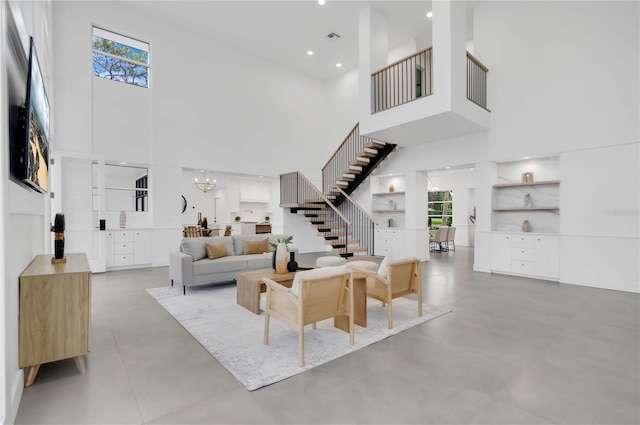 living room featuring a high ceiling, stairs, plenty of natural light, a chandelier, and concrete flooring
