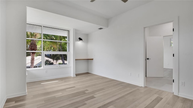 spare room featuring healthy amount of natural light, wood finished floors, a ceiling fan, and baseboards
