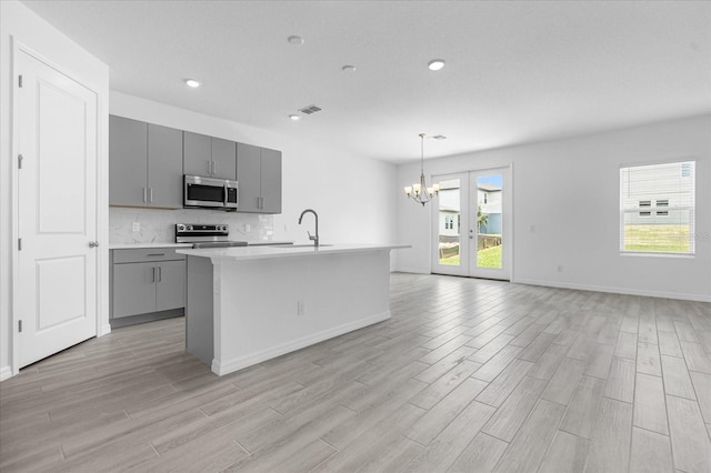 kitchen featuring gray cabinetry, a sink, backsplash, appliances with stainless steel finishes, and a chandelier