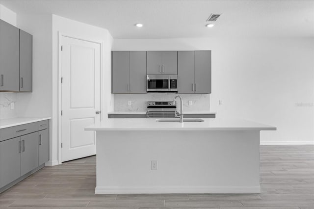 kitchen with gray cabinetry, light countertops, light wood-style floors, stainless steel appliances, and a sink