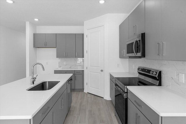 kitchen with gray cabinets, a sink, decorative backsplash, light countertops, and appliances with stainless steel finishes