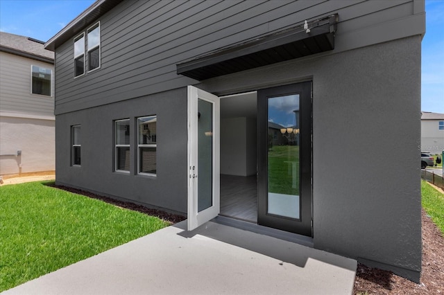 view of exterior entry with stucco siding and a lawn