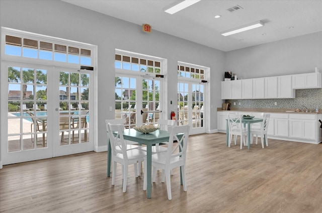 dining area featuring visible vents, a high ceiling, french doors, and light wood finished floors