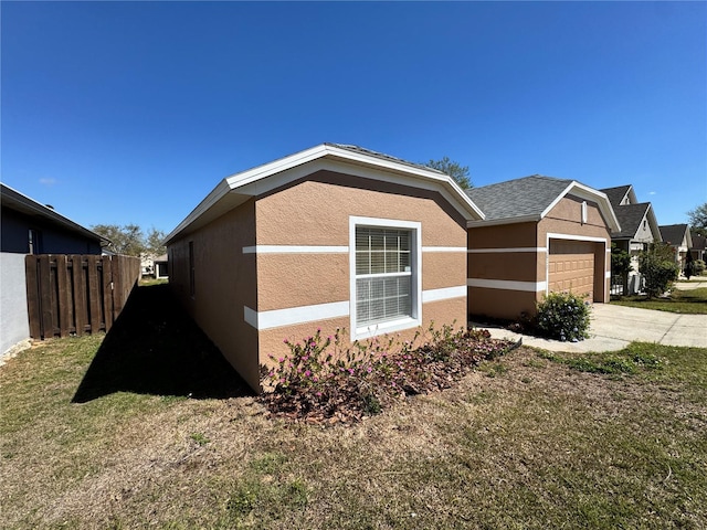 view of side of property with stucco siding, a lawn, fence, concrete driveway, and a shingled roof