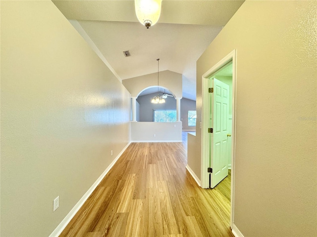 corridor with baseboards, visible vents, light wood-style flooring, vaulted ceiling, and a chandelier