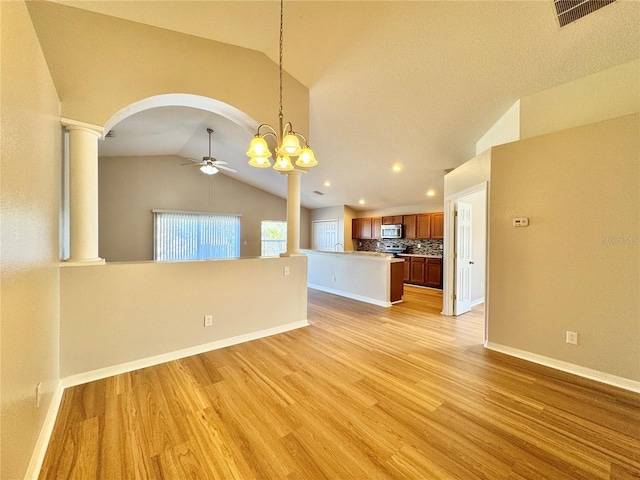 unfurnished living room featuring visible vents, ornate columns, vaulted ceiling, light wood-style floors, and ceiling fan with notable chandelier