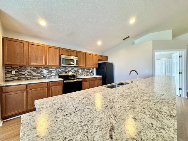 kitchen featuring visible vents, vaulted ceiling, brown cabinets, stainless steel appliances, and a sink