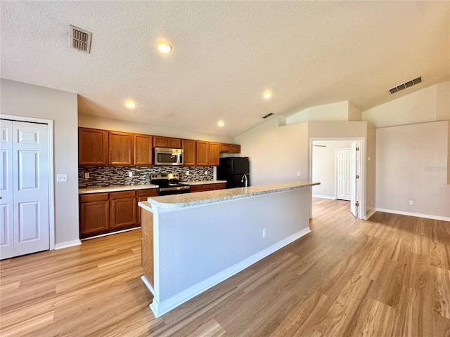 kitchen featuring brown cabinetry, visible vents, stainless steel appliances, and vaulted ceiling