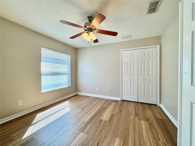 unfurnished bedroom with wood finished floors, visible vents, a closet, and baseboards