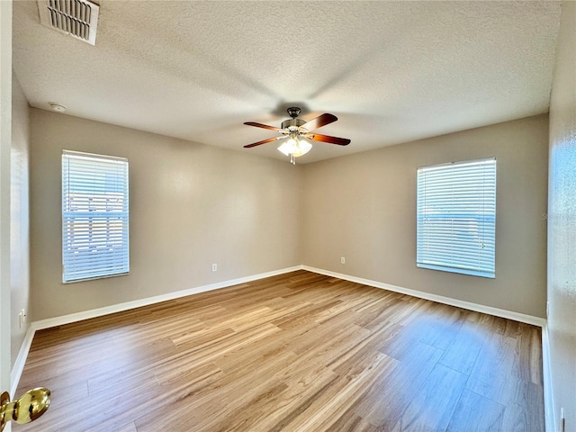 empty room with a ceiling fan, wood finished floors, visible vents, baseboards, and a textured ceiling