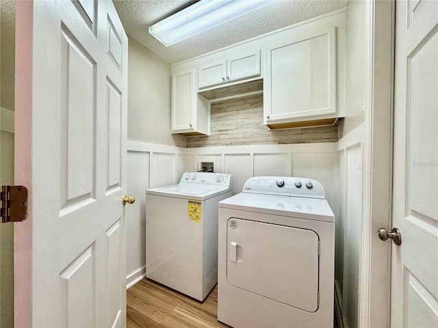 clothes washing area featuring wainscoting, washer and dryer, light wood-style floors, cabinet space, and a textured ceiling