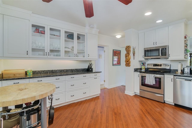 kitchen featuring stainless steel appliances, glass insert cabinets, light wood-style flooring, and a ceiling fan