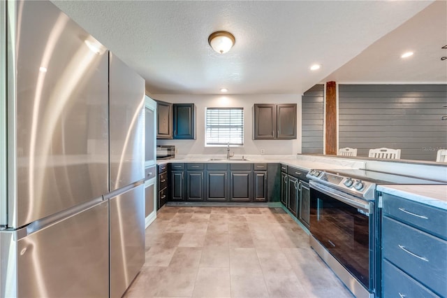 kitchen with a sink, a textured ceiling, recessed lighting, stainless steel appliances, and light countertops