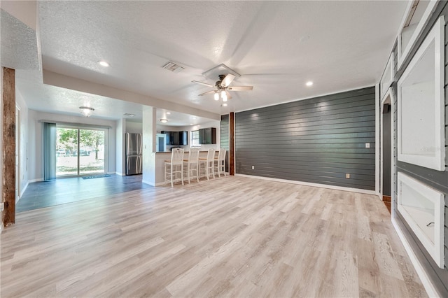 unfurnished living room featuring light wood finished floors, visible vents, baseboards, ceiling fan, and a textured ceiling