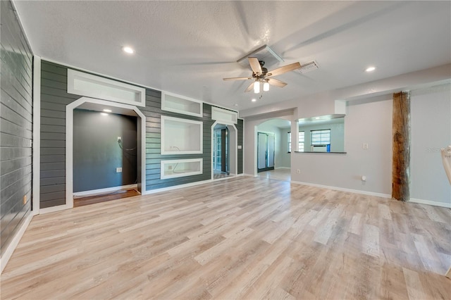 unfurnished living room featuring a ceiling fan, visible vents, light wood finished floors, arched walkways, and a textured ceiling