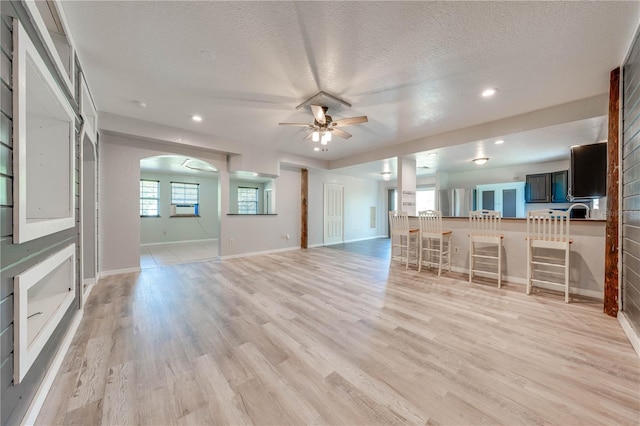 unfurnished living room with baseboards, ceiling fan, light wood-style floors, arched walkways, and a textured ceiling