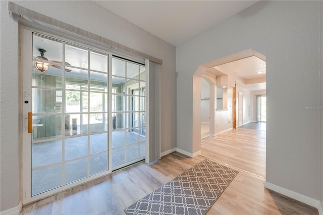 doorway to outside featuring arched walkways, ceiling fan, baseboards, and wood finished floors