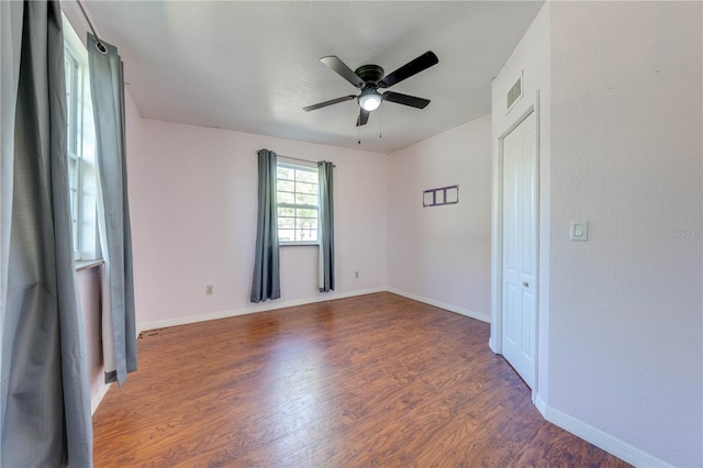 empty room with wood finished floors, a ceiling fan, visible vents, and baseboards