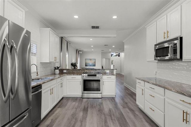 kitchen featuring a peninsula, stainless steel appliances, wood finished floors, white cabinetry, and a sink